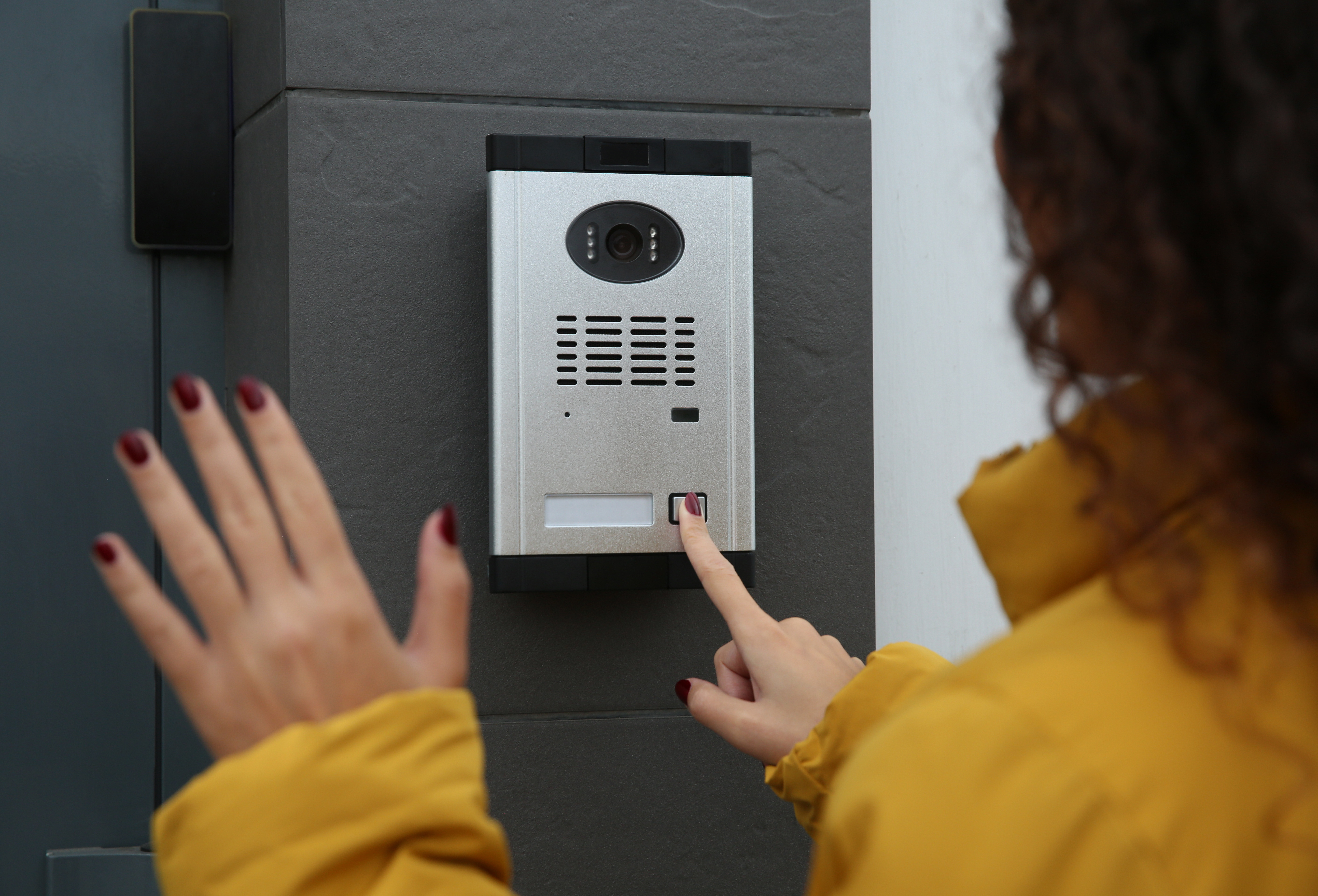 African-American woman ringing intercom while waving to camera near building entrance particuliers_masecurite_initiale